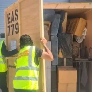 Movers in high-visibility vests securing a packed wooden storage crate filled with furniture and boxes – illustrating expert packing and storage services.