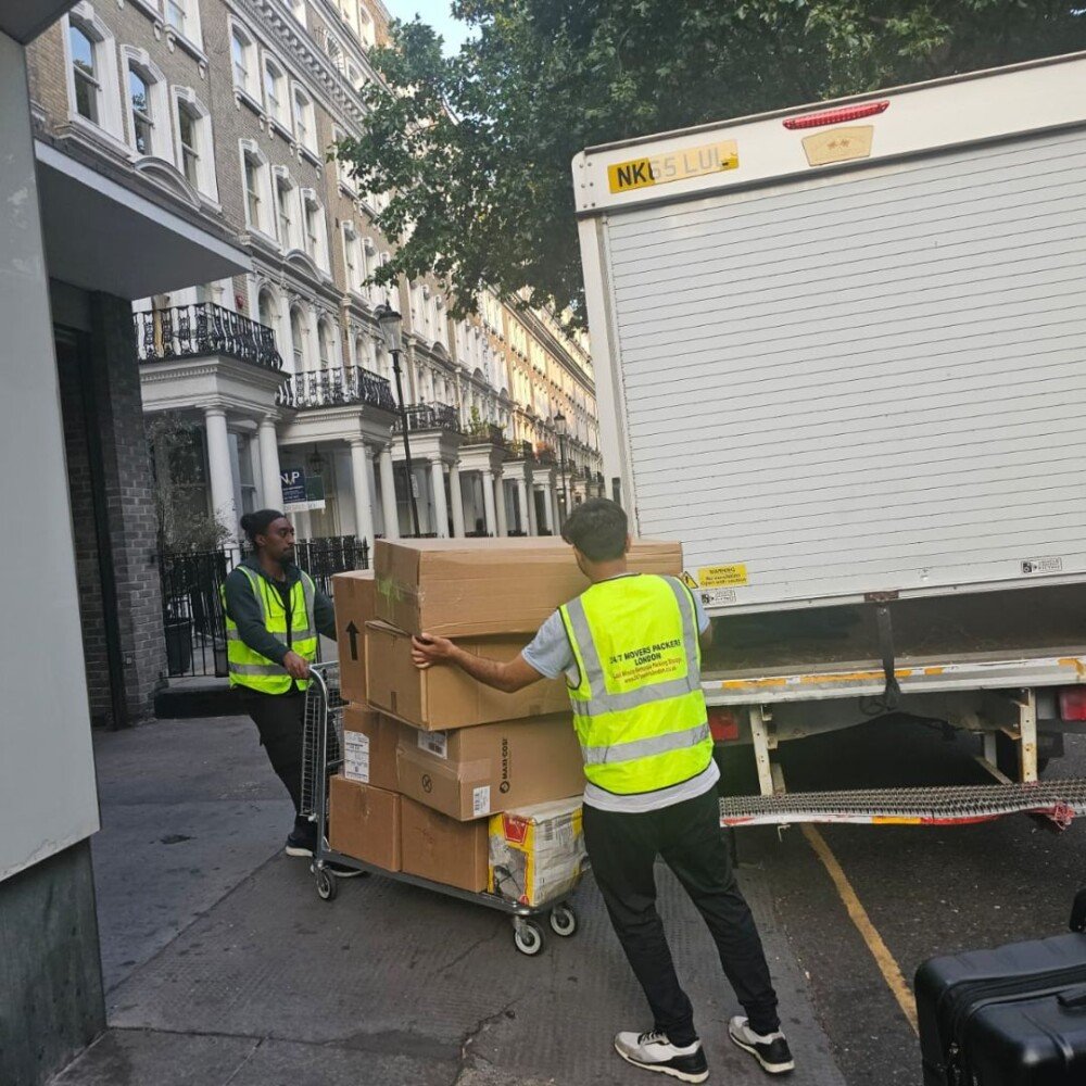 Two workers of 24/7 Movers Packers London are loading packed boxes into moving trolleys