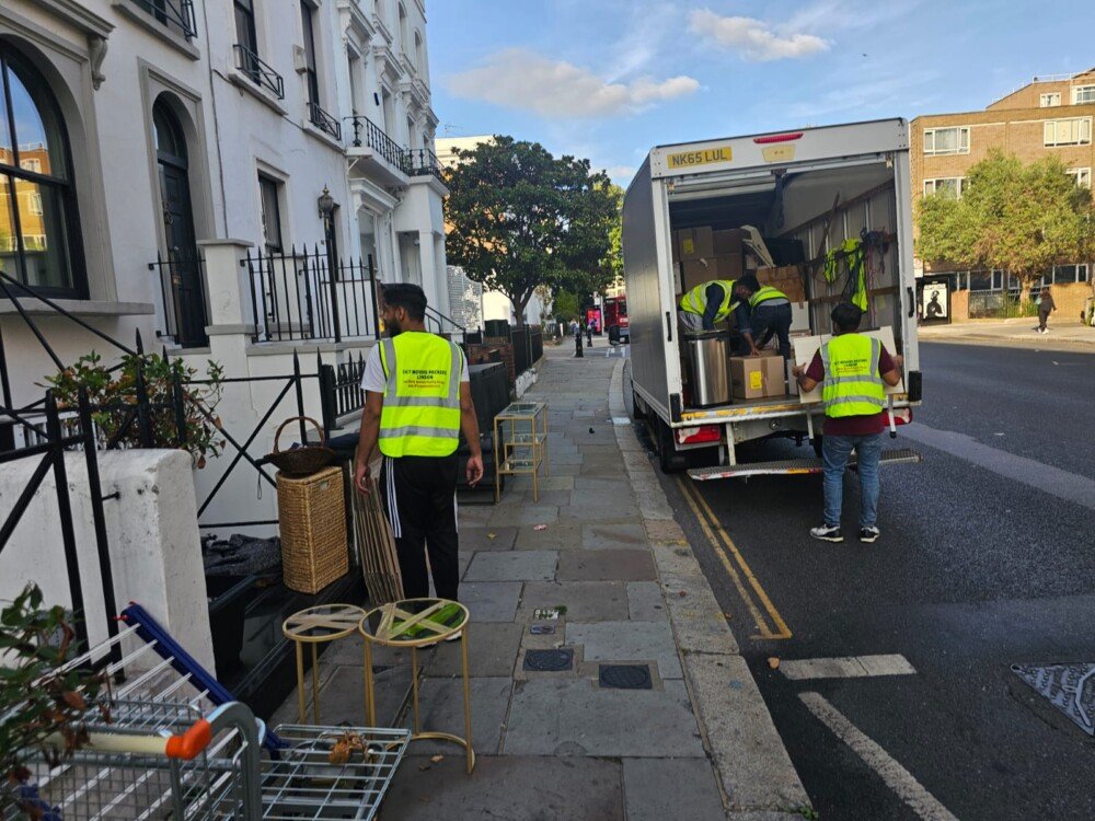 Several movers unloading furniture and boxes from a moving truck parked on the side of a city street.