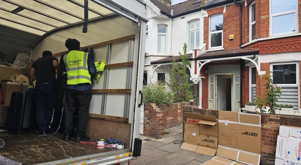 Movers loading boxes and furniture into a moving truck outside a residential house, Allied moving boxes on the pavement.