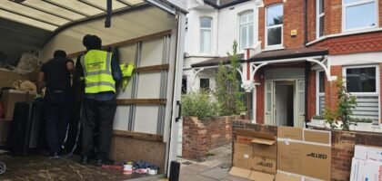 Movers loading boxes and furniture into a moving truck outside a residential house, Allied moving boxes on the pavement.