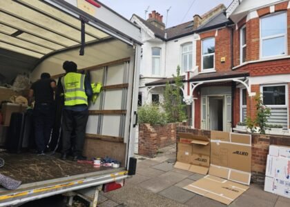 Movers loading boxes and furniture into a moving truck outside a residential house, Allied moving boxes on the pavement.
