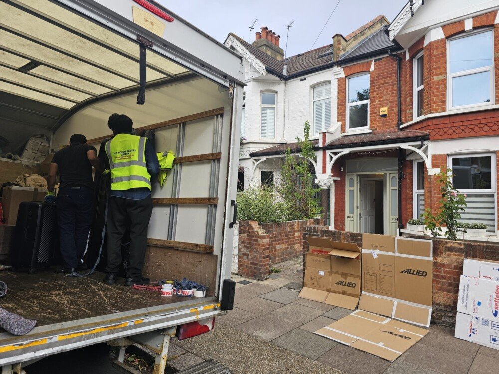Movers loading boxes and furniture into a moving truck outside a residential house, Allied moving boxes on the pavement.