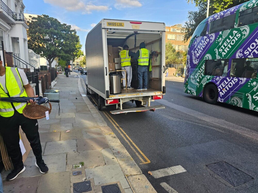 Moving team loading household items into a van parked on a London street, with a double-decker bus passing by.